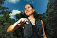 Load image into Gallery viewer, Woman wearing a black vest outdoors with trees and blue sky in the background
