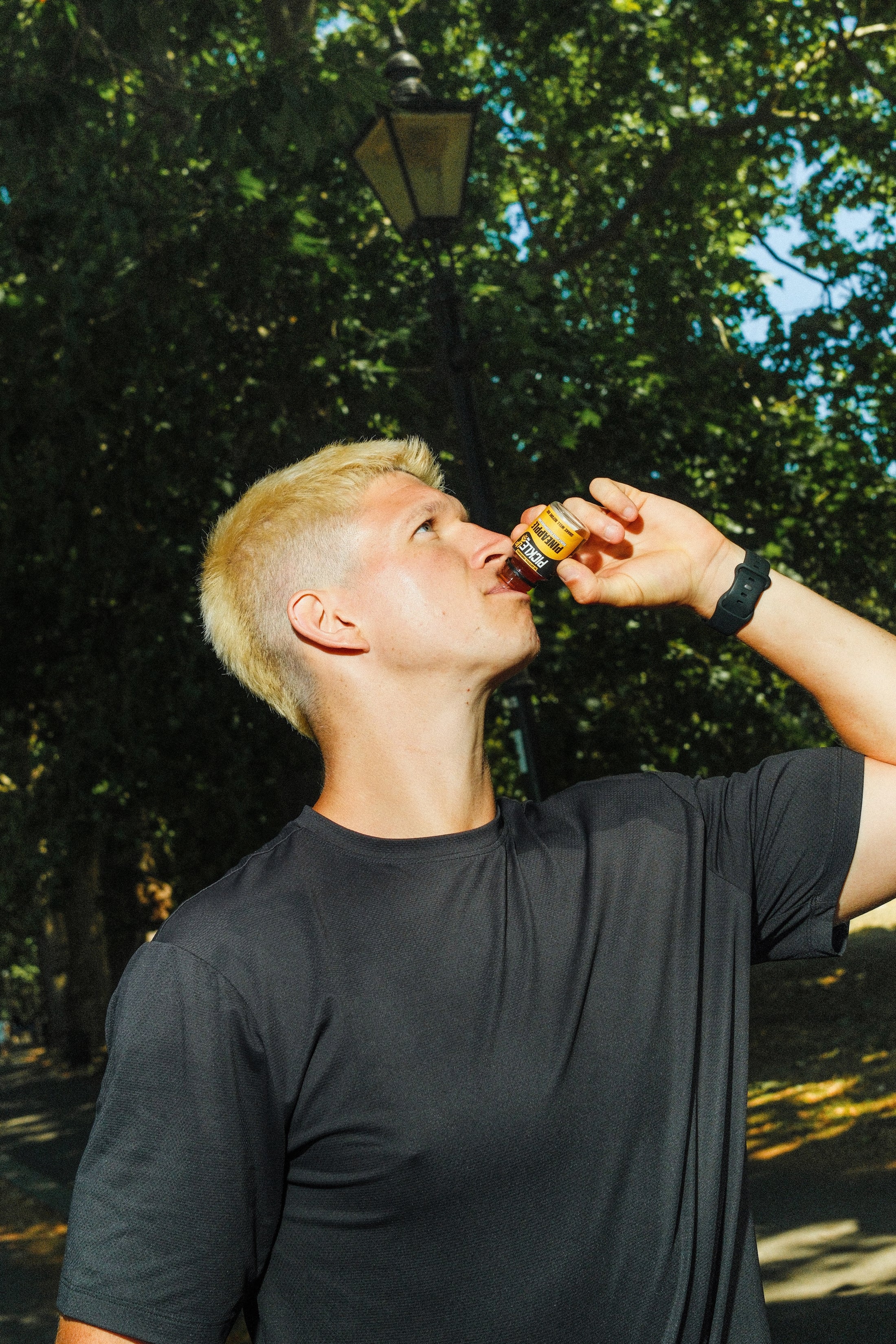 Man drinking from a PickleUp Pro bottle outdoors with trees in the background